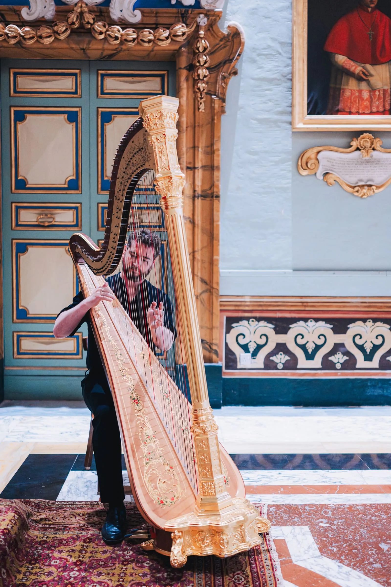 A harpist plays an ornately gilded harp beneath a cardinal's portrait in St Paul's Cathedral.