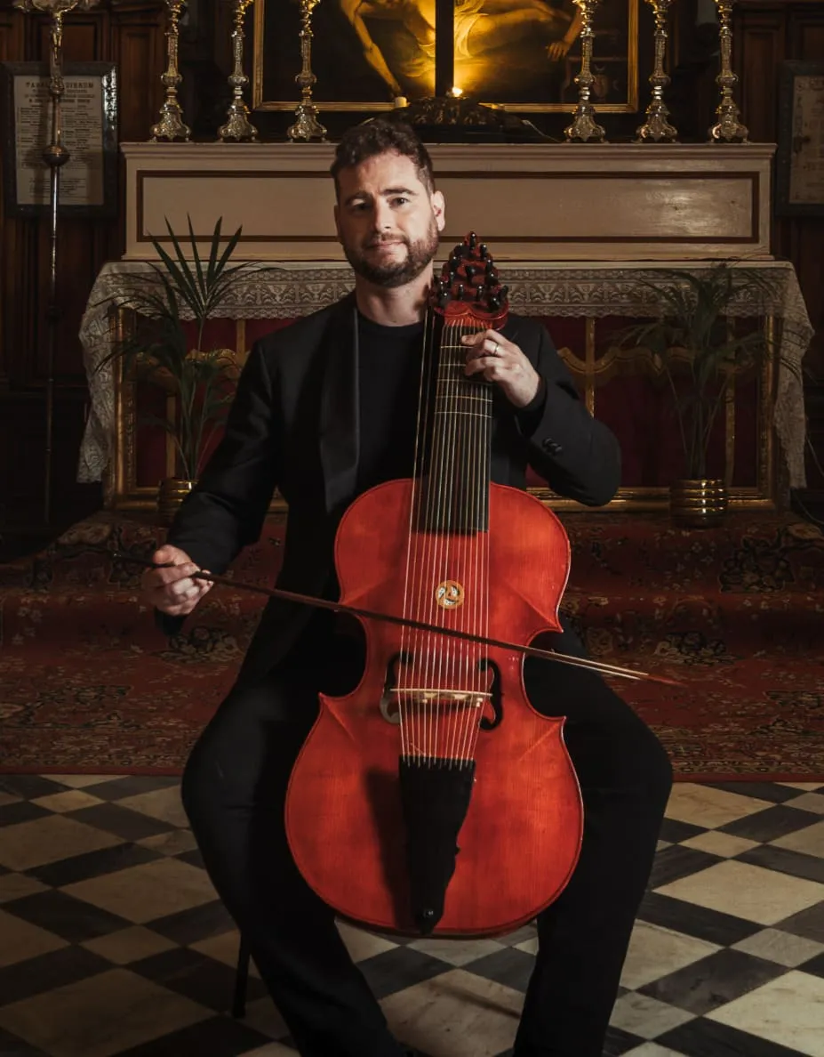 Jacob Portelli playing a Baroque bass viol before the altar, bow in hand.